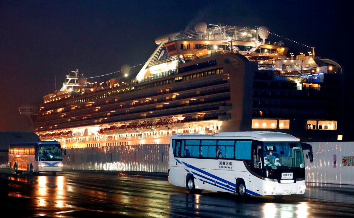 Buses carrying U.S. passengers who were aboard the quarantined cruise ship the Diamond Princess, seen in background, leaves Yokohama port near Tokyo early on Feb. 17, 2020. (Jun Hirata/Kyodo News via AP)