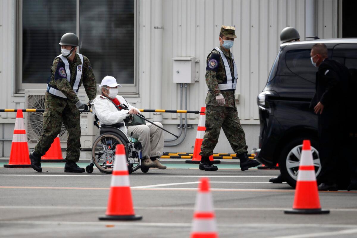An unidentified passenger on a wheelchair is escorted after he disembarked from the quarantined Diamond Princess cruise ship in Yokohama, near Tokyo on Feb. 19, 2020. (Jae C. Hong/AP Photo)