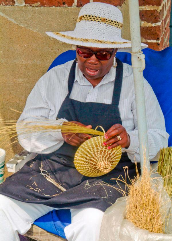 A woman sews a sweet grass basket for sale outside Charleston’s old market building. (Fred J. Eckert)