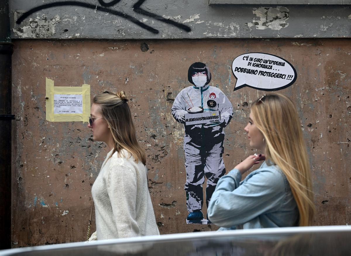 Two women walk by a mural painting reading "There's an epidemic of ignorance in the air, we must protect ourselves!" referring to the coronavirus outbreak by the street artist Laika near the Chinese district in Rome, Italy, on Feb. 4, 2020. (Filippo Monteforte/AFP via Getty Images)