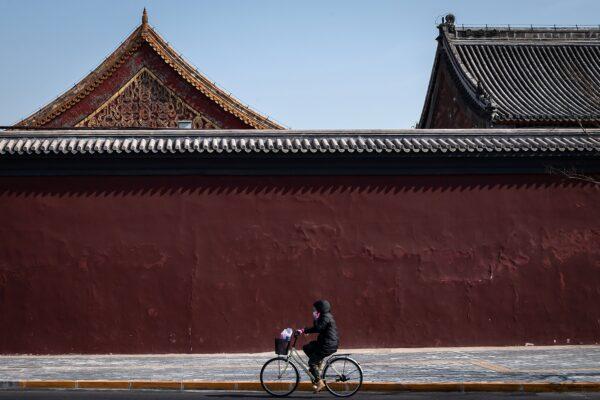 A woman wearing a protective facemask to protect against the COVID-19 coronavirus cycles on a nearly empty street close to the Lama Temple which is closed off to the public in Beijing, China on Feb. 23, 2020. (NICOLAS ASFOURI/AFP via Getty Images)