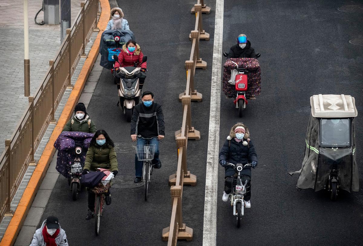 Chinese commuters, all wearing protective masks, ride bikes and scooters as they cross an intersection in rush hour in Beijing, China, on Feb. 24, 2020. (Kevin Frayer/Getty Images)