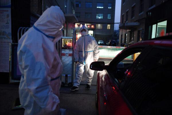 Two security guards wear protective clothing as a preventive measure against the COVID-19 coronavirus as they question a driver before taking his temperature at the entrance to a restaurant in Beijing on Feb. 25, 2020. (Greg Baker/AFP via Getty Images)