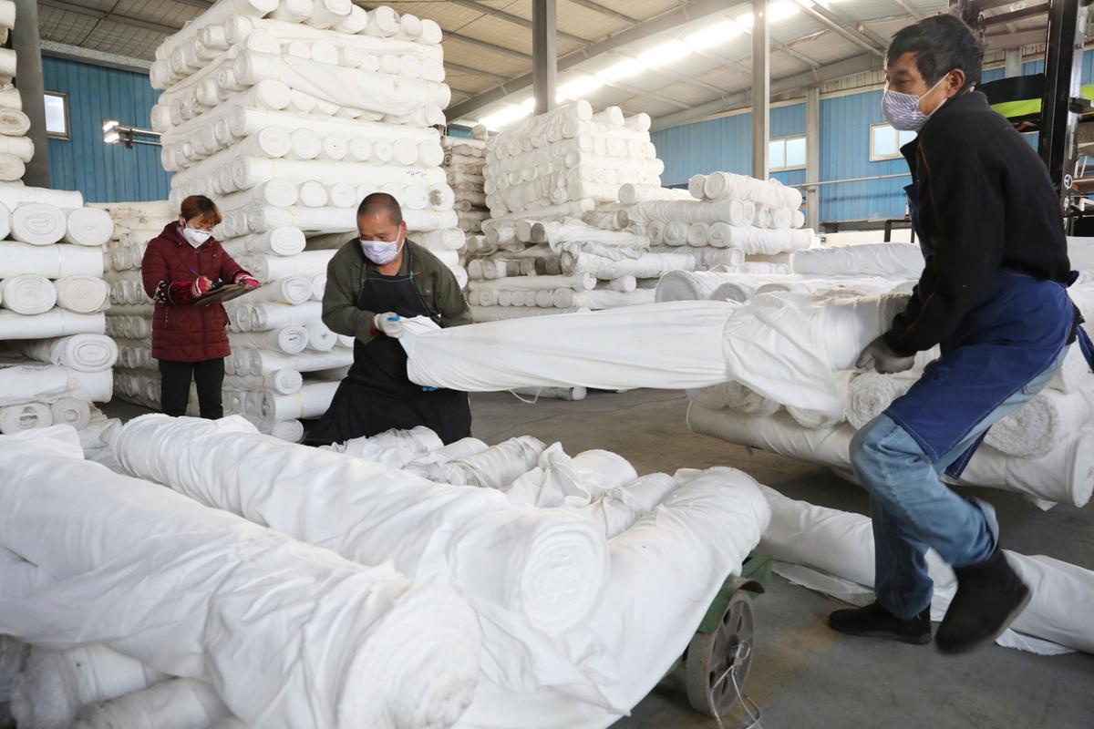 Workers wearing masks move fabric rolls at a textile printing and dyeing plant in Hangzhou in eastern China's Zhejiang Province on Feb. 20, 2020. (Chinatopix Via AP)