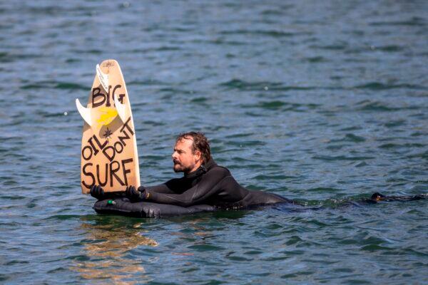 A man holds up a board reading "Big oil don't surf" during a surf demonstration, a so-called paddle-out, taking place on May 12, 2019, in the harbor pool outside the Opera House in Oslo, Norway, against a planned oil exploration of Norwegian multinational energy company Equinor in the The Great Australian Bight. (OLA VATN/AFP via Getty Images)