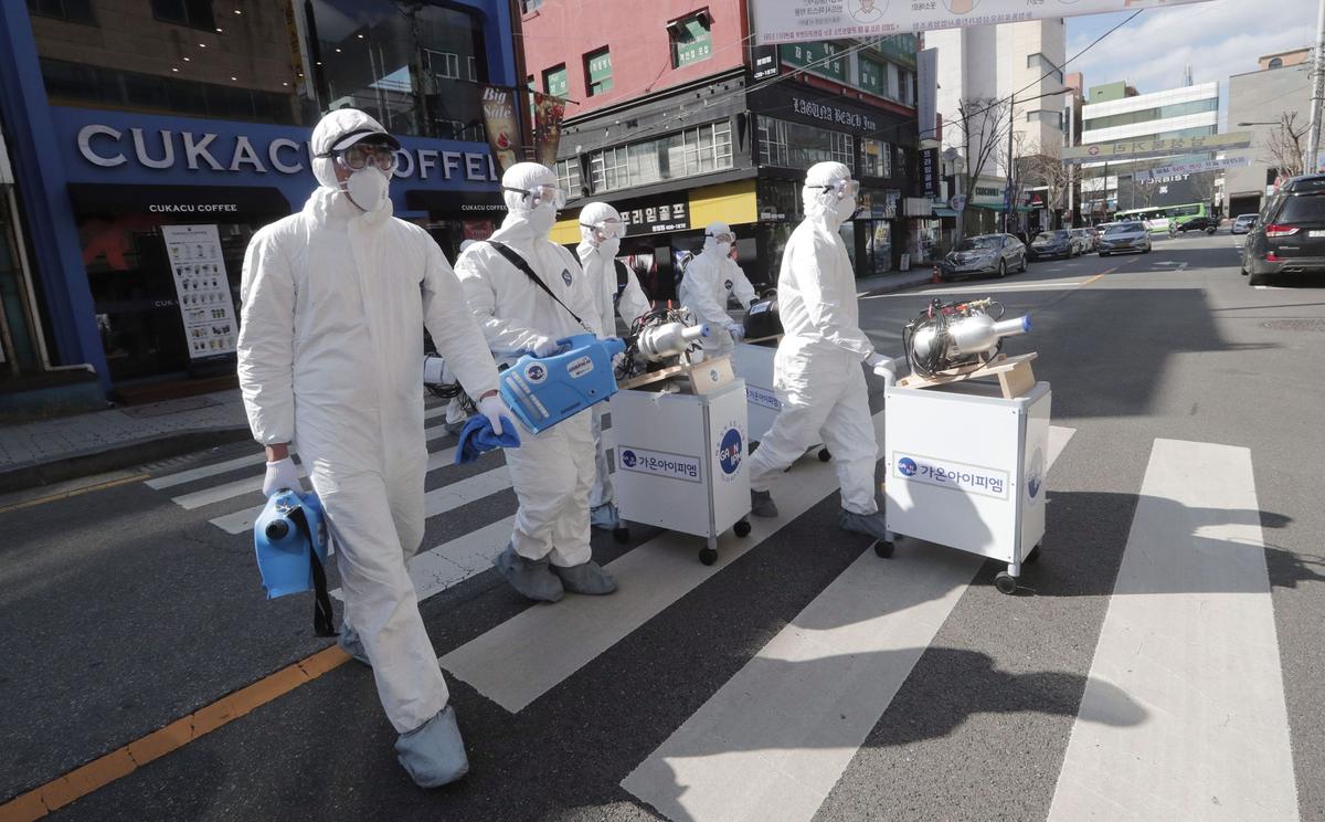 Workers wearing protective gear arrive to spray disinfectant as a precaution against the new coronavirus at a shopping street in Seoul, South Korea, on Feb. 27, 2020. (AP Photo/Ahn Young-joon)