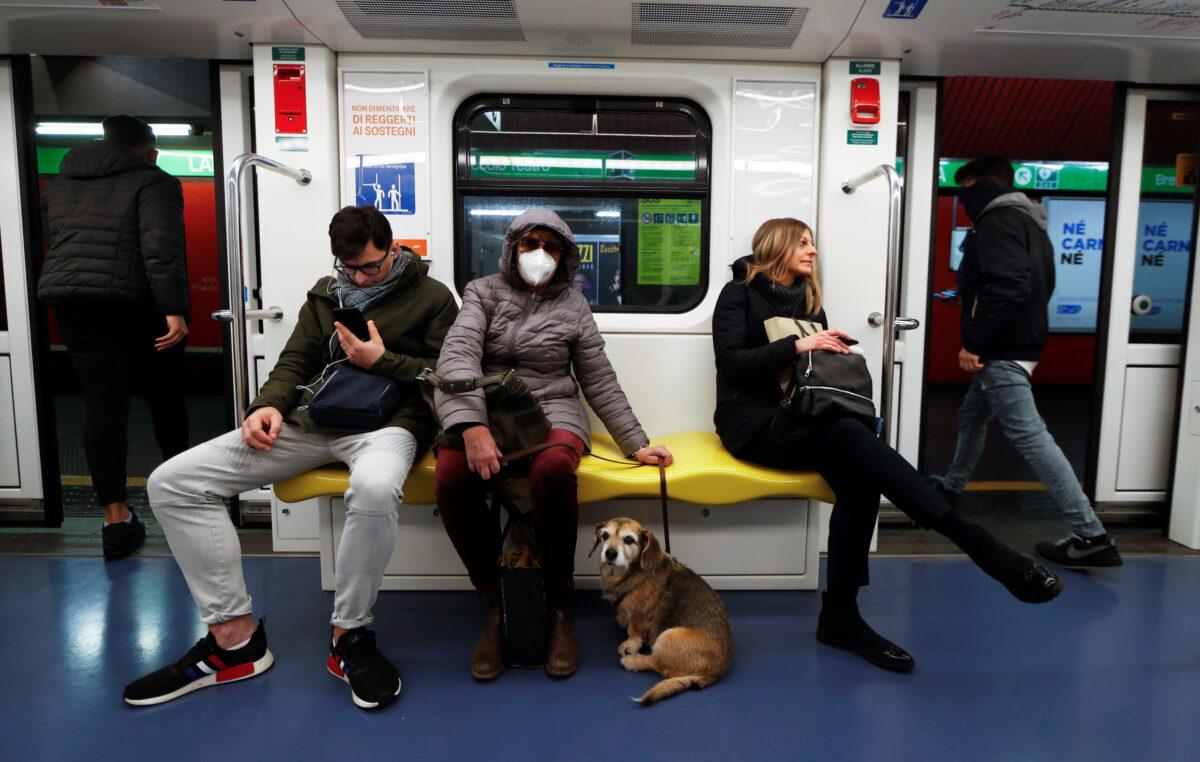 A woman wearing a protective mask and her dog sit on the subway in Milan, Italy, on March 1, 2020. (Yara Nardi/Reuters)