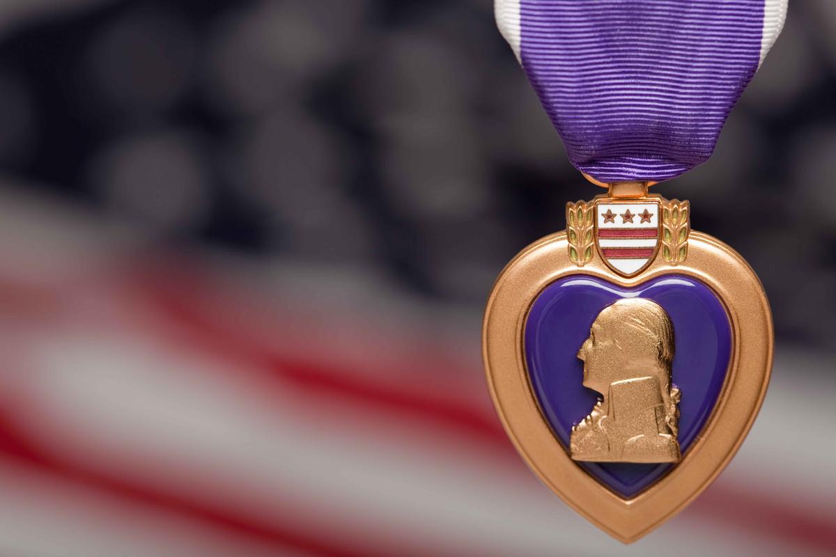 Illustration - Shutterstock | <a href="https://www.shutterstock.com/image-photo/purple-heart-against-blurry-american-flag-30245284">Andy Dean Photography</a>