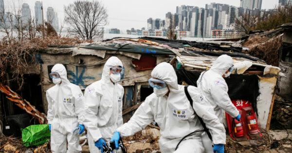 South Korean soldiers in protective gear sanitize shacks as a luxury high-rise apartment complex is seen in the background at Guryong village in Seoul, South Korea, on March 3, 2020. (Heo Ran/Reuters)