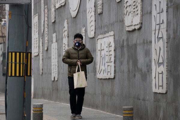 A resident wearing a mask walks outside a closed school with a mural depicting keywords including at right "Rule of law" in Beijing, on Feb. 25, 2020. (AP Photo/Ng Han Guan)