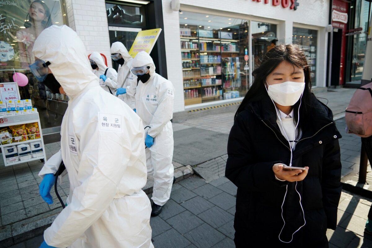 A woman wearing a mask as a preventive measure against the coronavirus walks past South Korean soldiers in protective gear sanitizing a street in Seoul on March 5, 2020. (Kim Hong-Ji/Reuters)