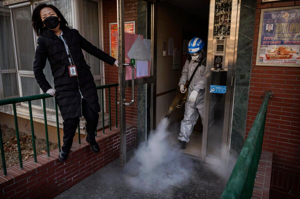 A Chinese volunteer from Blue Sky Rescue wears a protective suit as he uses fumigation equipment to disinfect common areas of a local residential compound as a member of the community opens the door for him in Beijing, China on March 5, 2020. (Kevin Frayer/Getty Images)