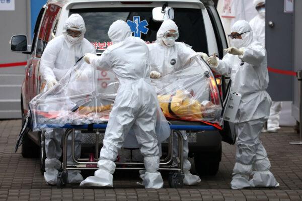 Medical staff wearing protective gear move a patient infected with the CCP virus from an ambulance to a hospital in Seoul on March 9, 2020. (Chung Sung-Jun/Getty Images)