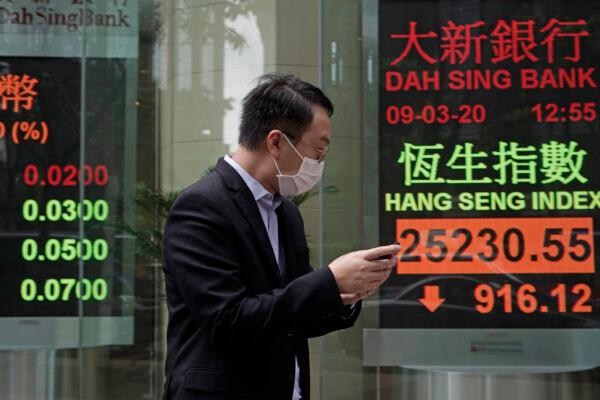 A man walks past an electronic board showing Hong Kong share index outside a local bank in Hong Kong, on March 9, 2020. (Kin Cheung/AP Photo)