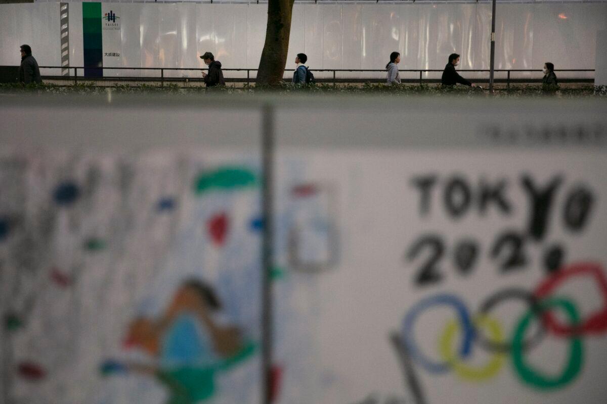 In this March 3, 2020, file photo, commuters walk along a sidewalk as a poster celebrating the Tokyo 2020 Olympics is seen in foreground in Tokyo. (Jae C. Hong/AP Photo)