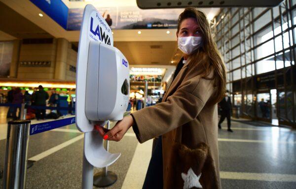 A woman wearing a mask uses hand sanitizer on arrival at Los Angeles International Airport on March 12, 2020. (Frederic J. Brown/AFP via Getty Images)