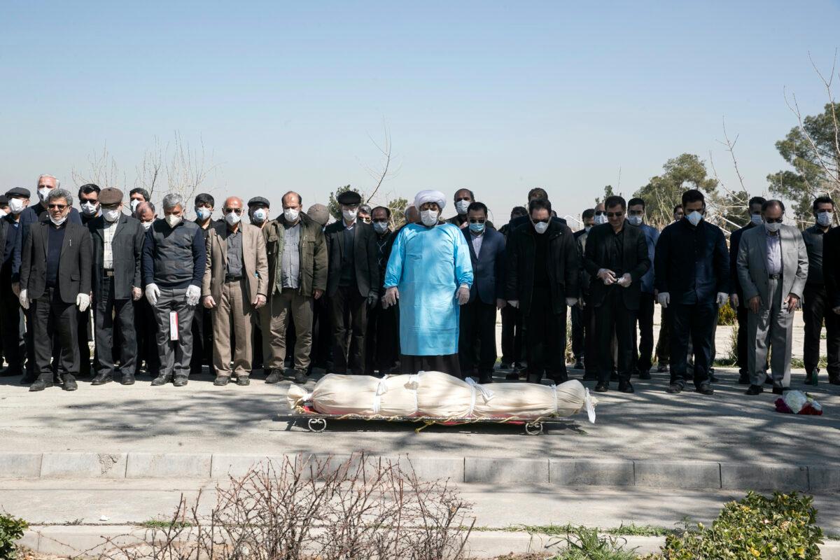 Mourners wearing face masks and gloves pray over the body of former politburo official in the Revolutionary Guard Farzad Tazari, who died Monday after being infected with the new coronavirus, at the Behesht-e-Zahra cemetery just outside Tehran, Iran on Tuesday, March 10, 2020. (Mahmood Hosseini/Tasnim News Agency via AP)