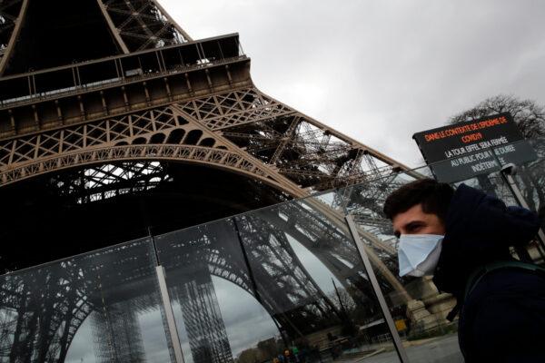 A man wearing a mask walks pasts the Eiffel tower closed after the French government banned all gatherings of over 100 people to limit the spread of the virus COVID-19, in Paris, on March 14, 2020. (Christophe Ena/AP Photo)