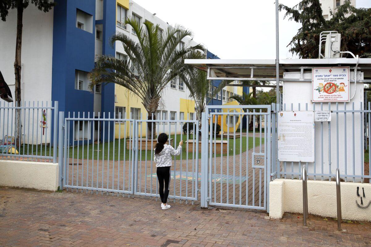 A child stands at the locked gate of a school in the central Israeli coastal city of Netanya, a day after an announcement made by the Israeli prime minister of the closure of schools and universities as a preventive measure to limit the spread of the coronavirus COVID-19, on March 13, 2020. (Jack Guez/AFP via Getty Images)