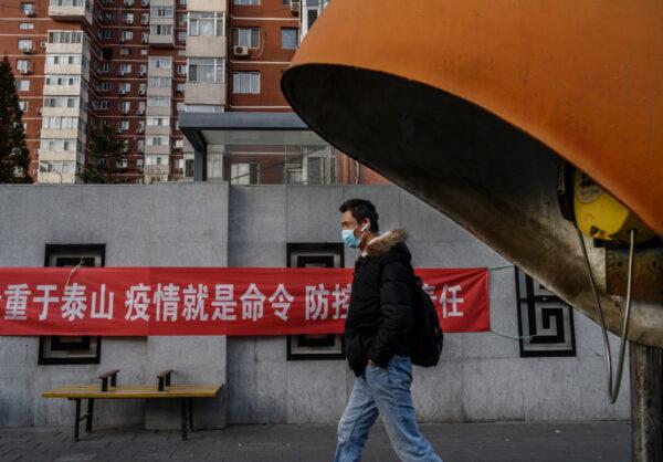 A Chinese man wears a protective mask as he walks by a propaganda banner related to the coronavirus outbreak on a residential building in Beijing, China, on Feb. 21, 2020. (Kevin Frayer/Getty Images)