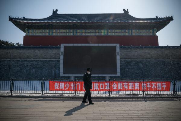 A security guard walks past a banner saying "Do Not Leave Home Often During Holidays, Wear a Mask When Going Out, Keep a Distance and Do Not Shake Hands When Meeting" in Temple of Heaven Park, Beijing, on Feb. 15, 2020. (Andrea Verdelli/Getty Images)
