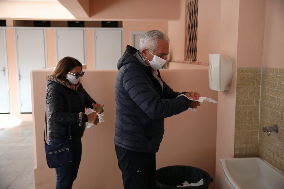 A couple wearing face masks wipe their hands after voting, in Menton, France, on March 15, 2020. (Daniel Cole/AP Photo)