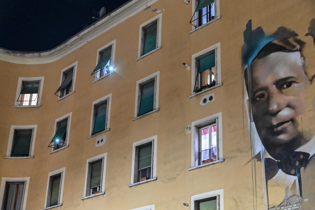 People watch through their windows during a flash mob, "Italia Patria Nostra" ("Italy Our Country"), in Rome's Garbatella district on March 15, 2020. (©Getty Images | <a href="https://www.gettyimages.com/detail/news-photo/people-hold-smartphoness-lights-from-their-window-during-a-news-photo/1207242500?adppopup=true">ANDREAS SOLARO</a>)