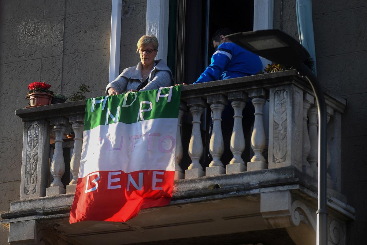 A woman places an Italian flag that reads "everything will be alright" on her apartment balcony as part of a flashmob organized to raise morale during Italy's CCP virus crisis, in Milan, Italy, on March 16, 2020. (Daniele Mascolo/Reuters)