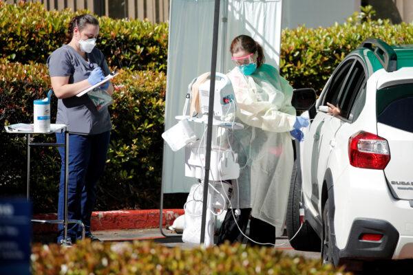 A health care worker attends to a person at a drive-up care facility in response to the outbreak of COVID-19, in La Jolla, Calif., on March 17, 2020. (Mike Blake/Reuters)