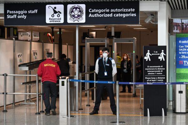 An airport security staff, wearing a respiratory mask (C), waits to control passengers at Rome's Fiumicino international airport on March 13, 2020. (Andreas Solaro/AFP)