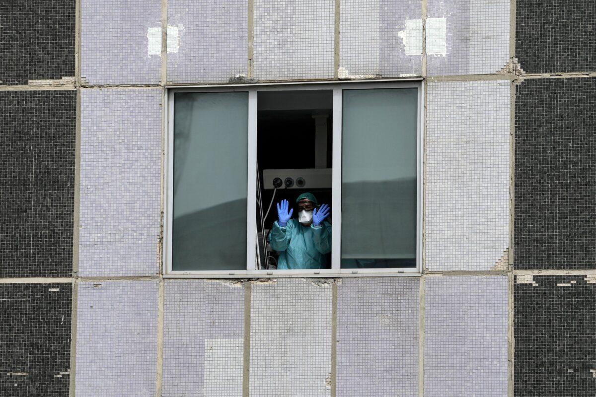 A health worker in a full protective suit and a mask waves from a window of La Paz hospital in Madrid on March 18, 2020. (Oscar Del Pozo/AFP via Getty Images)