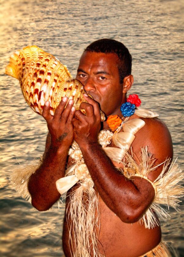 A Fijian blows into a shell used as a horn to announce an event at an island resort in Fiji. (Copyright Fred J. Eckert)