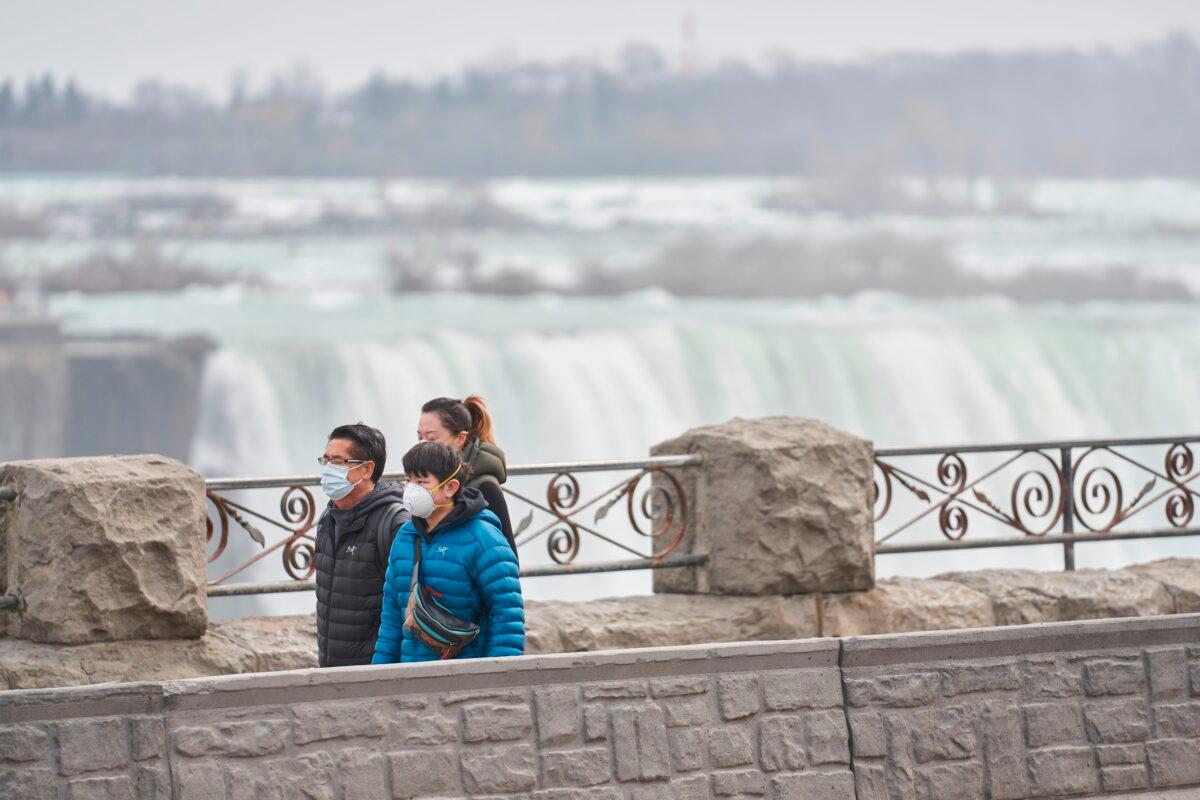 Tourists in masks walk past the Horseshoe Falls in Niagara Falls, Ontario, Canada, on March 18, 2020. (Geoff Robins/AFP via Getty Images)