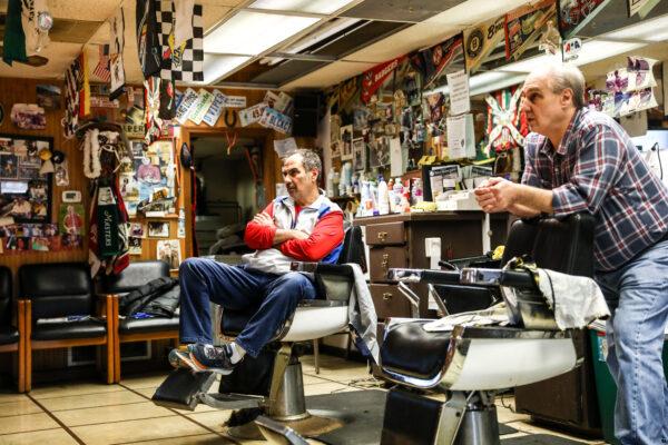 Barbers and brothers Tommy (L) and Jimmy Checkler watch the latest news on the coronavirus in their empty barbershop in the City of Worthington in Columbus,Ohio, on March 17, 2020. (Charlotte Cuthbertson/The Epoch Times)