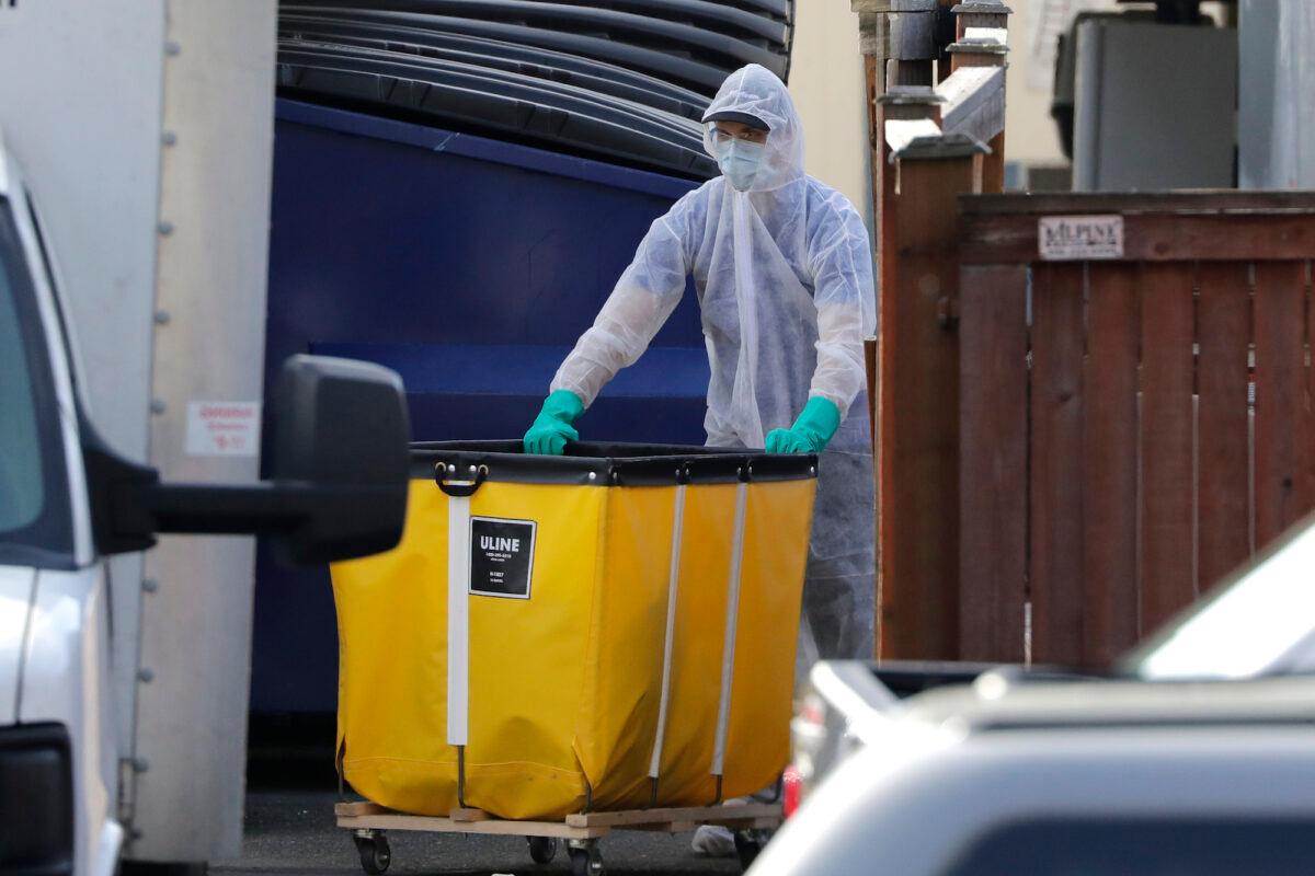 A member of a cleaning crew wheels a cart toward a vehicle at the Life Care Center, in Kirkland, Wash. on March 18, 2020. (AP Photo/Elaine Thompson)