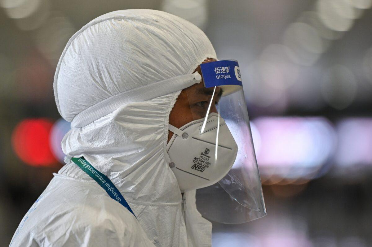 An airport security staff member wearing protective gear amid concerns over the COVID-19 outbreak waits for passengers to escort them to a bus at Shanghai Pudong International Airport in Shanghai on March 19, 2020. (Hector Retamal/AFP via Getty Images)