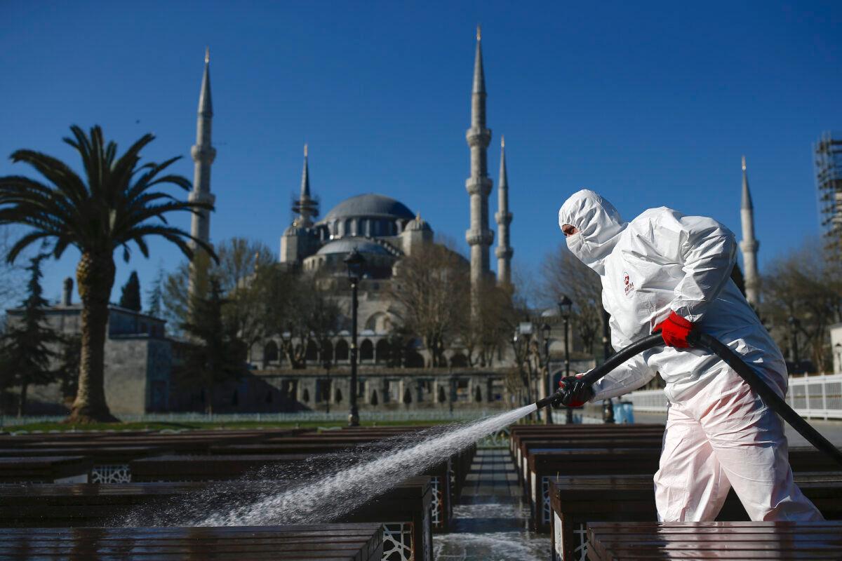 A worker wearing a face mask and protective suits disinfects chairs amid the coronavirus outbreak, in Istanbul, Turkey, on March 21, 2020. (AP Photo/Emrah Gurel)