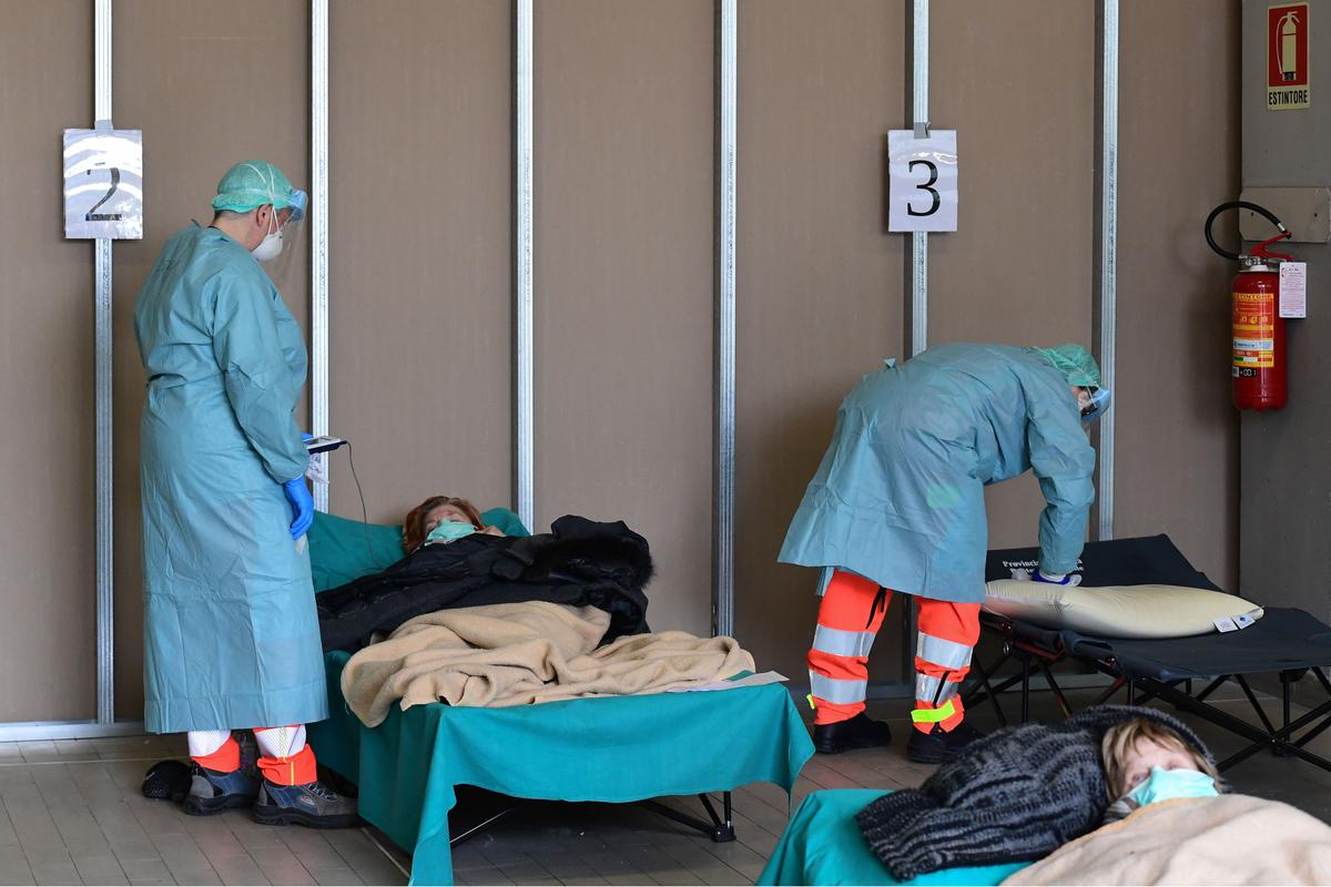 Hospital employees wearing masks and gear tend to patients lying in bed at a temporary emergency structure set up outside the accident and emergency department, where any new arrivals presenting suspect new coronavirus symptoms will be tested, at the Brescia hospital, Lombardy, Italy, on March 13, 2020. (Photo by Miguel MEDINA / AFP)