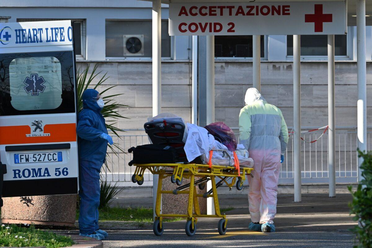 Male nurses wearing face masks and overalls bring a patient on a stretcher into the newly built Columbus Covid 2 temporary hospital to fight the new coronavirus infection at the Gemelli hospital in Rome on March 16, 2020. (Andreas Solano/AFP via Getty Images)