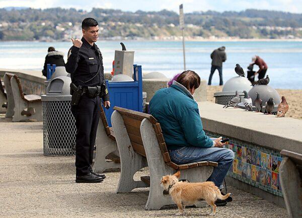 Police Sgt. Leo Moreno tells a couple they have to keep moving and can't sit on the Esplanade bench explaining that the bench may have the coronavirus on it in Capitola, Calif., on March 25, 2020. (Dan Coyro/The Santa Cruz Sentinel via AP)