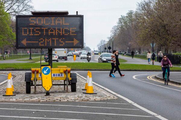 A sign notifies passersby of the 2-meter social distancing measures in place, as people exercise in Phoenix Park in Dublin, after Ireland introduced measures to help slow the spread of the CCP virus, on March 25, 2020. (Paul Faith/AFP via Getty Images)