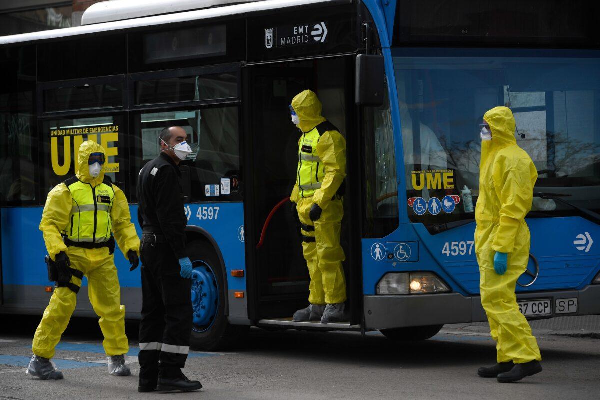 Members of Spanish Military Emergencies Unit (UME) wearing protective suits stand outside a bus used to transport patients from the San Carlos Clinic Hospital to a temporary hospital set-up for CCP virus patients at the Ifema convention and exhibition center in Madrid, on March 29, 2020. (Pierre-Philippe Marcou/AFP via Getty Images)