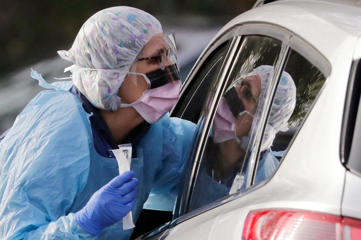 In this March 17, 2020, file photo, Laurie Kuypers, a registered nurse, reaches into a car to take a nasopharyngeal swab from a patient at a drive-thru COVID-19 testing station for University of Washington Medicine patients in Seattle. (Elaine Thompson/AP Photo)