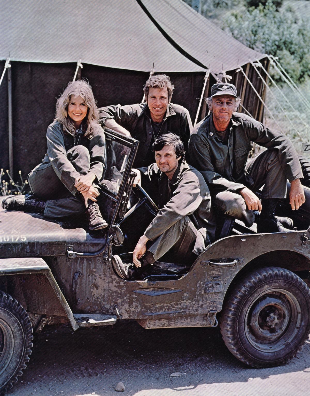 American actor, director, and writer Alan Alda in the driver's seat of a jeep, surrounded by Loretta Swit and other cast members of the hit television show M.A.S.H. (Keystone/Getty Images)