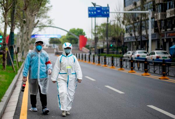 Two people, wearing protective suits as a preventive measure against the CCP virus, walk along a street in Wuhan, China on March 31, 2020. (NOEL CELIS/AFP via Getty Images)