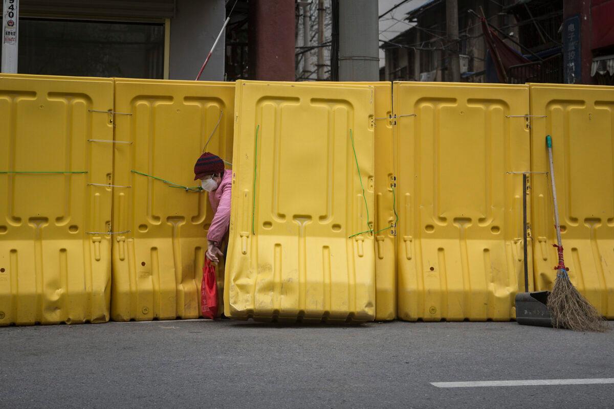 A woman wearing a face mask opens a makeshift barricade wall built to control entry and exit to a residential compound in Wuhan, China on March 31, 2020. (Getty Images)