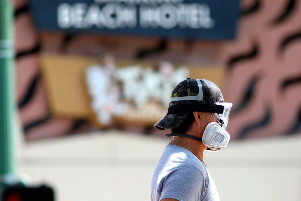 A man wears goggles and a mask as he walks a dog along Waikiki Beach in Honolulu on March 28, 2020. (Caleb Jones/AP Photo)
