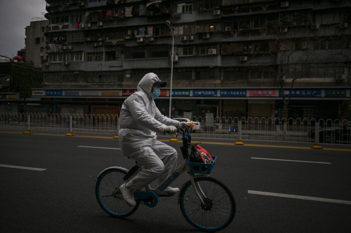 A man wearing a protective suit rides a bicycle on a street in Wuhan, China on April 1, 2020. (Hector Retamal/AFP via Getty Images)