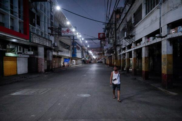 A man wearing a protective mask on his neck walks past closed shops in an empty street following the lockdown in the Philippine capital to prevent the spread of the CCP virus, in Manila, Philippines, on March 24, 2020. (Eloisa Lopez/Reuters)