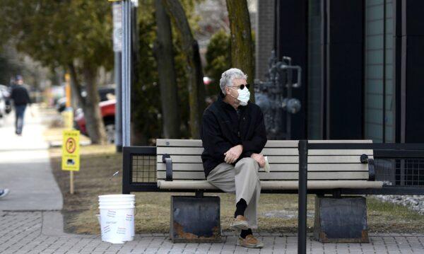 A man wears a mask for protection against COVID-19 while waiting outside a store in Ottawa, Canada, on April 4, 2020. (The Canadian Press/Justin Tang)